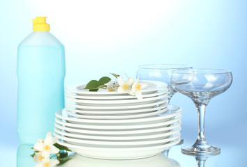 plates and glasses with cleaning liquid on blue background
