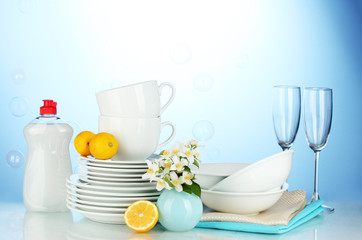 plates, glasses and cups with cleaning liquid on blue background
