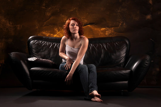 Eine junge Frau mit sichtbaren Nippeln auf schwarzem Ledersofa sitzend