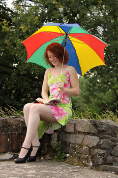 Eine Frau liest ein Buch im Garten unter Regenschirm sitzend
