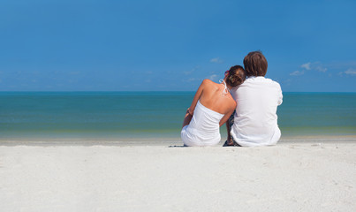 Young couple sitting on the beach looking on the horizon
