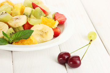 Fresh fruits salad on plate and berries on white wooden table