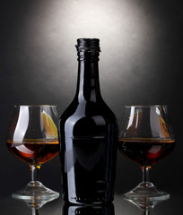 Glasses of brandy and bottle on gray background