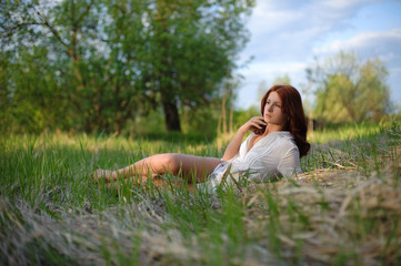 Fototapeta na wymiar A beautiful girl with red hair lies in the grass