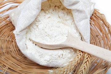 Flour and wheat grain with wooden spoon on a wicker basket.