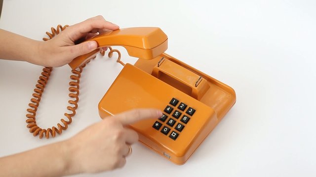 Woman is pressing the buttons of old orange telephone