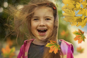 little girl in autumn with falling leaves and hair in wind