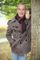 Senior man leaning against a tree