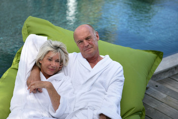 Elderly couple lying on inflatable mattress on a pool deck