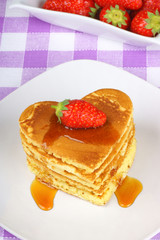 Stack of heart-shaped pancakes with syrup and strawberry