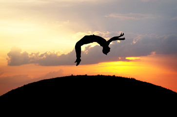 silhouette of gymnast jumping on hill in sunset