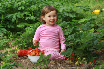 Kleinkind sitzt in einem Erdbeerbeet