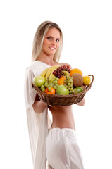 A young woman in white holding a basket full of fruits