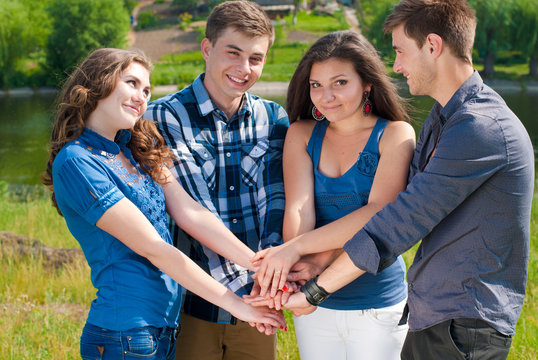 Group of four teenagers shaking hands and smiling outdoors