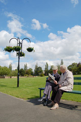 Senior couple sitting on a park bench reading a newspaper