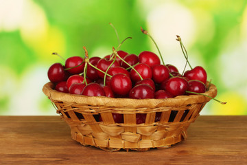 cherry in wicker bowl on wooden table on green background
