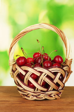 cherry in basket on wooden table on green background