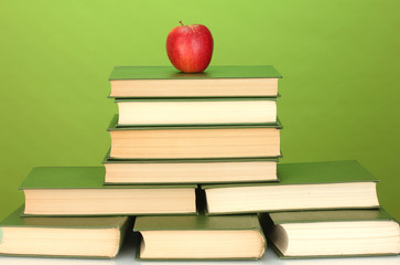 pile of books with apple on green background close-up