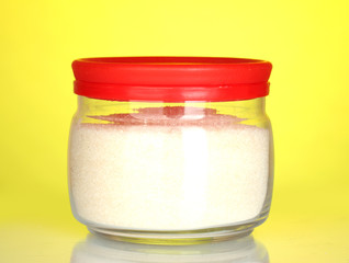 Jar with white crystal sugar on colorful background