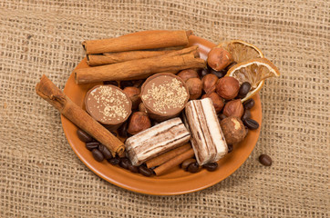 Sweets, cinnamon, nuts and coffee beans on a saucer, on burlap b
