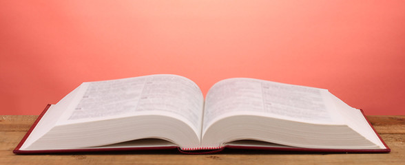 Open book on wooden table on red background