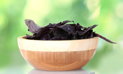 Basil in a wooden bowl on bright green background