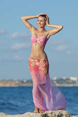 Girl in pink sarong with arms raised on the beach