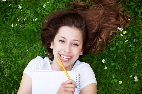 Young woman outdoors with workbook and pencil