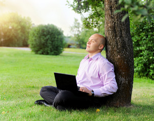 Businessman with laptop sitting near a tree