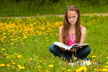 A girl 11 years old reads a book in the meadow