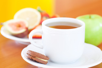 cup of tea,cookie,apple, lemon, fig and strawberries on a plate