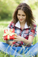 Beautiful teen girl with gift in the park at green grass.