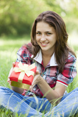 Beautiful teen girl with gift in the park at green grass.