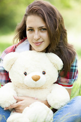 Beautiful teen girl with Teddy bear in the park at green grass.