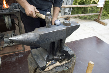 Ein Schmied bearbeitet ein kleines Werkstück mit dem Schmiedehammer