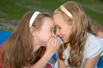 Two sisters, laughing, talking about something secret.