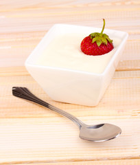 Glass of ripe strawberries with cream on wooden background