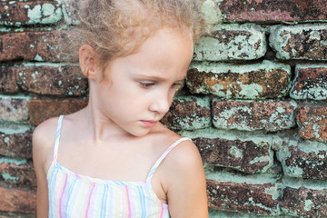 sad little girl on the background of an old brick wall