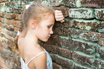 sad little girl on the background of an old brick wall