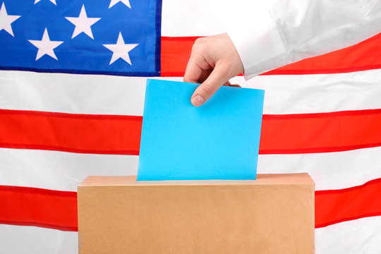 Hand with voting ballot and box on Flag of USA