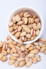 Bowl of pistachios spilling out on white background