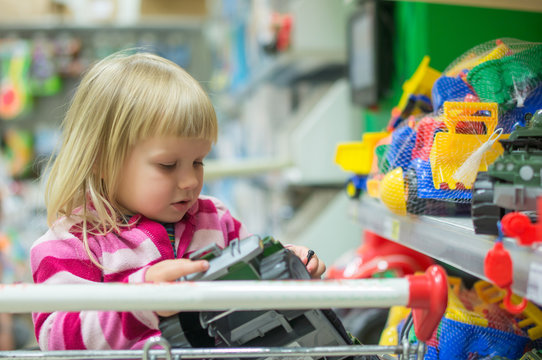 Adorable girl look to toys sit in shopping cart in supermarket