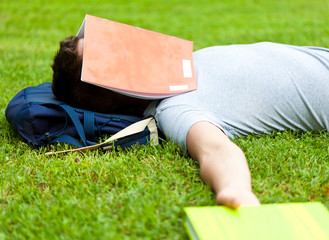 Tired student sleeping with a book over is face at the park
