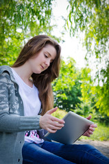 Girl working on a tablet in the green park summer
