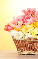 beautiful tulips in basket on wooden table on yellow background.
