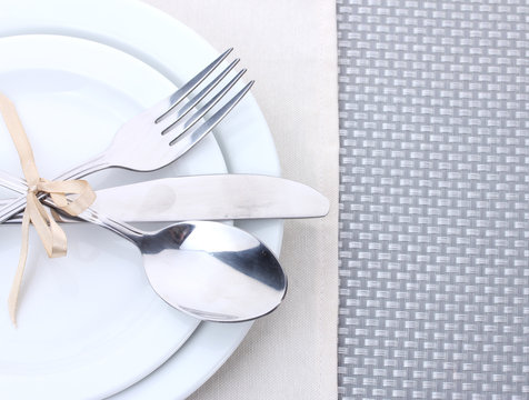 White empty plates with fork, spoon and knife tied with a ribbon
