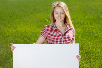 Young woman holding blank whiteboard, on grass background