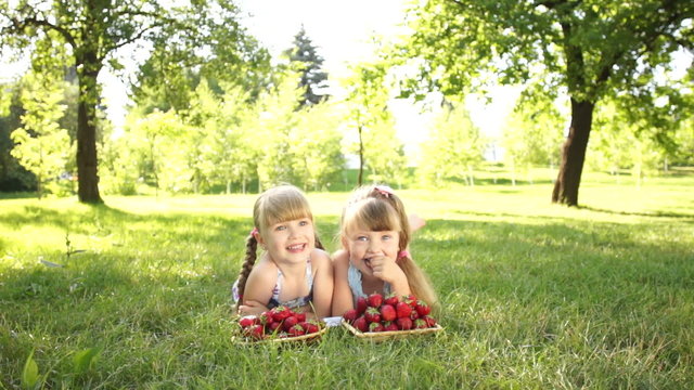 Laughing children lie on the grass. They eat strawberries