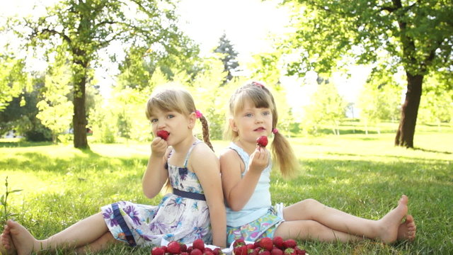 Happy kids eat strawberries. Sitting on the grass. Dolly HD