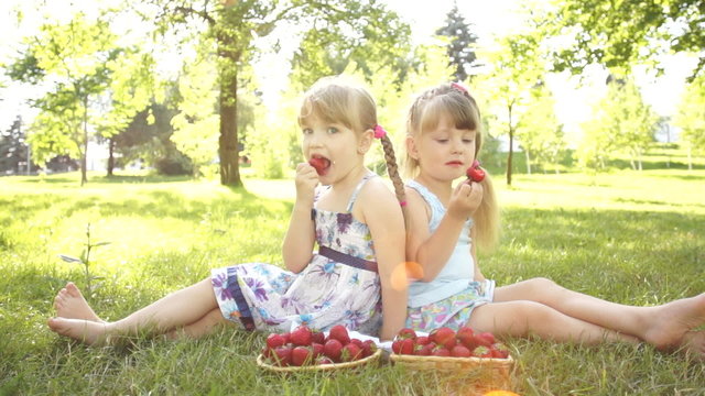 Happy girls eating strawberries. Sitting on the grass.